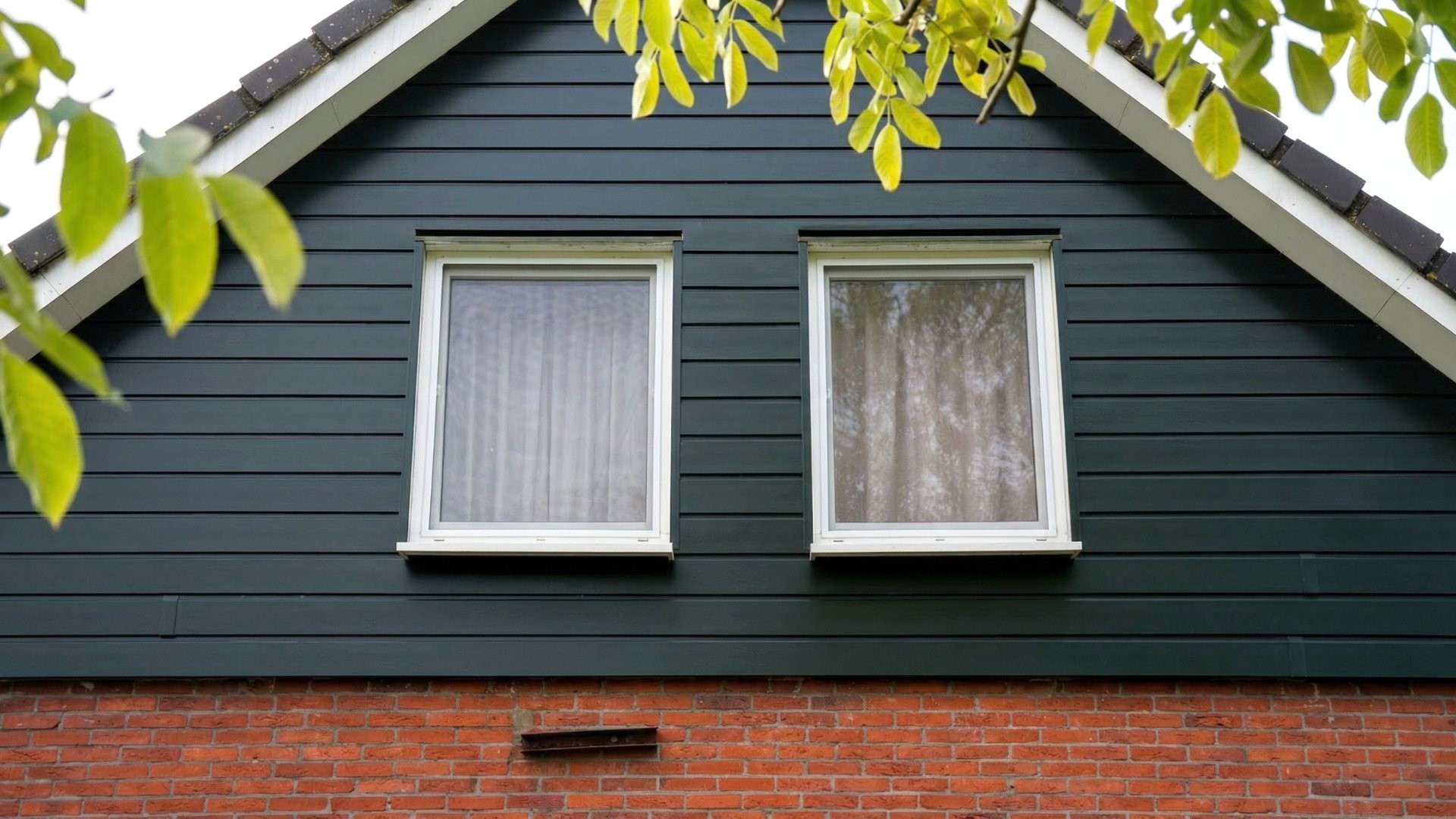 VinyPlus groen op topgevel met twee ramen en bladeren op de voorgrond
